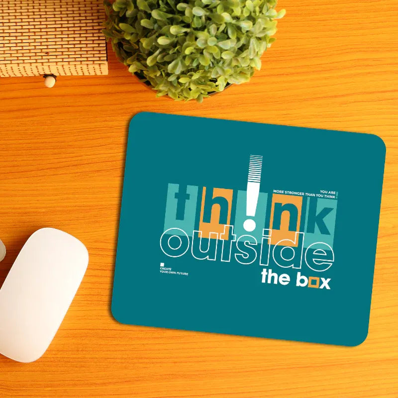 Teal mouse pad with 'think outside the box' text on a wooden surface with a plant and white mouse.