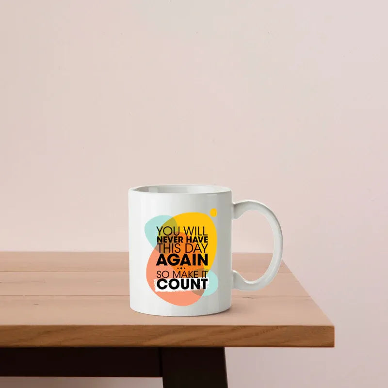 White mug with colorful text on a wooden table against a light pink background