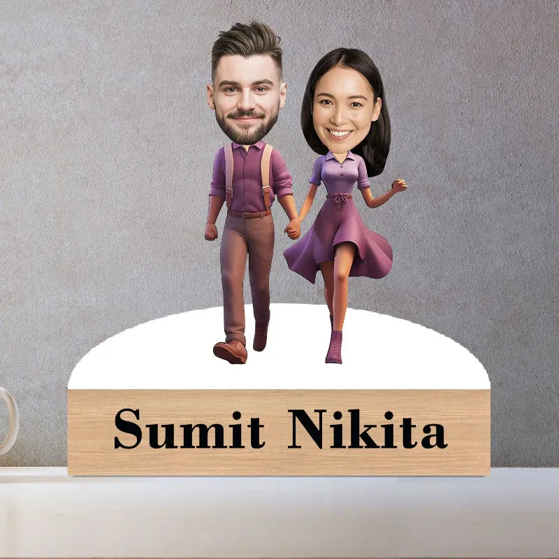 Bobblehead figures of a man and woman holding hands with a wooden plaque below displaying 'Sumit Nikita' on a gray background.