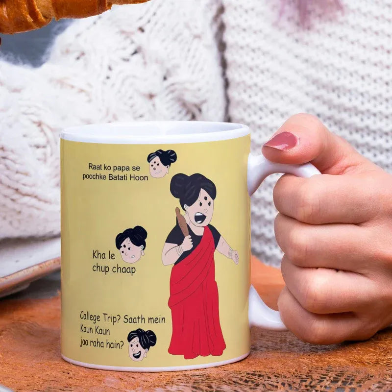 Mug with cartoon design and text held by a hand on a wooden surface.