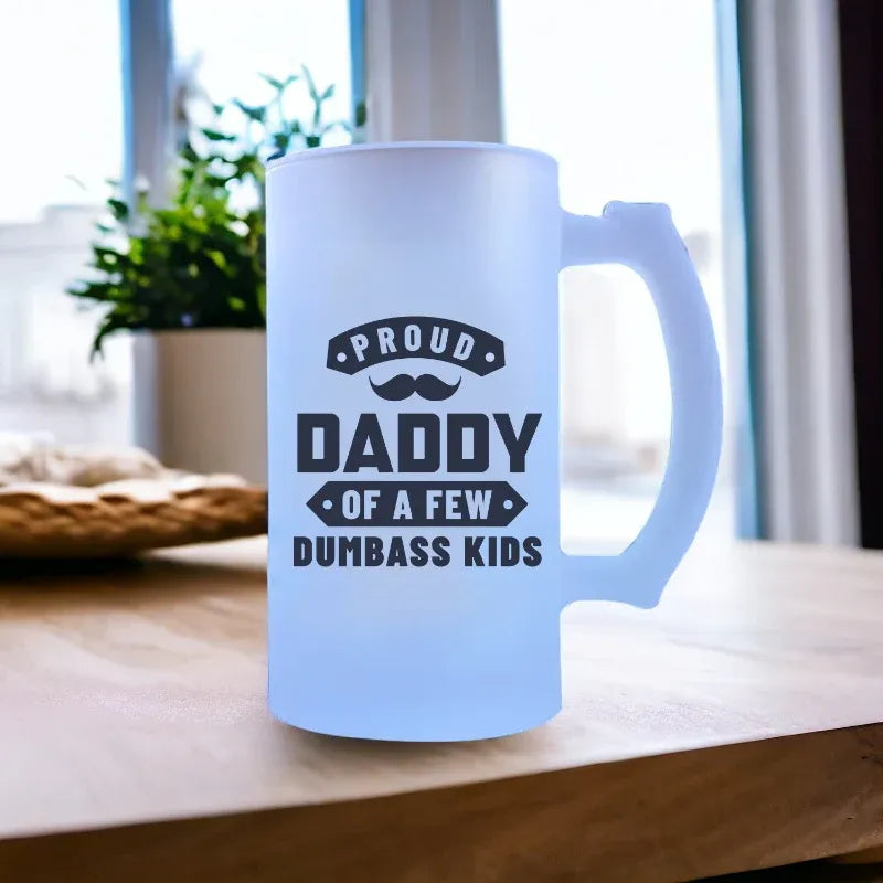 Frosted mug with text 'Proud Daddy of a Few Dumbass Kids' on a wooden surface.