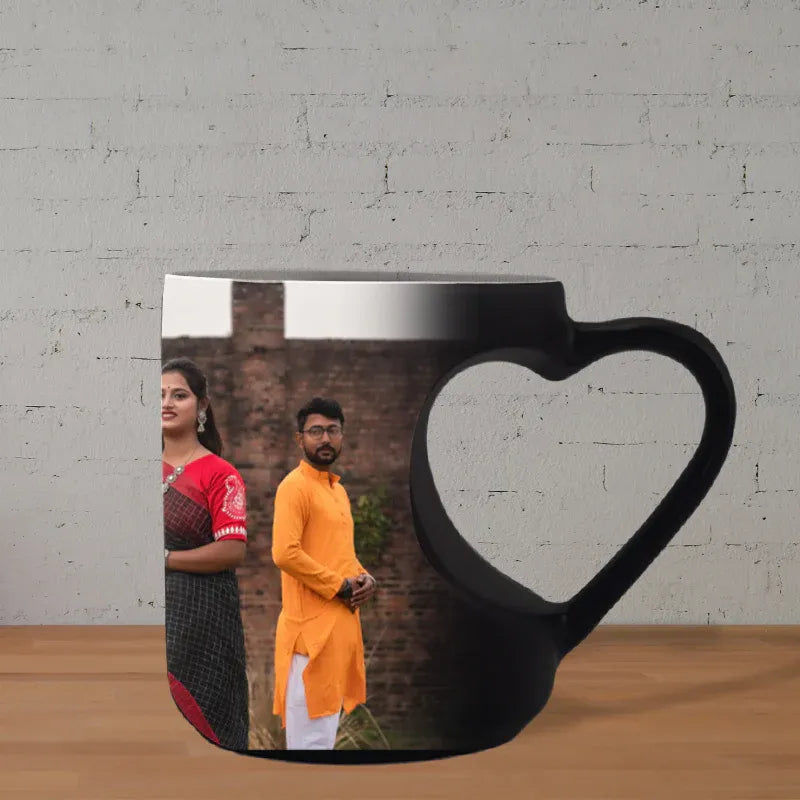 Black mug with a heart-shaped handle featuring a printed image of a couple on a wooden surface.