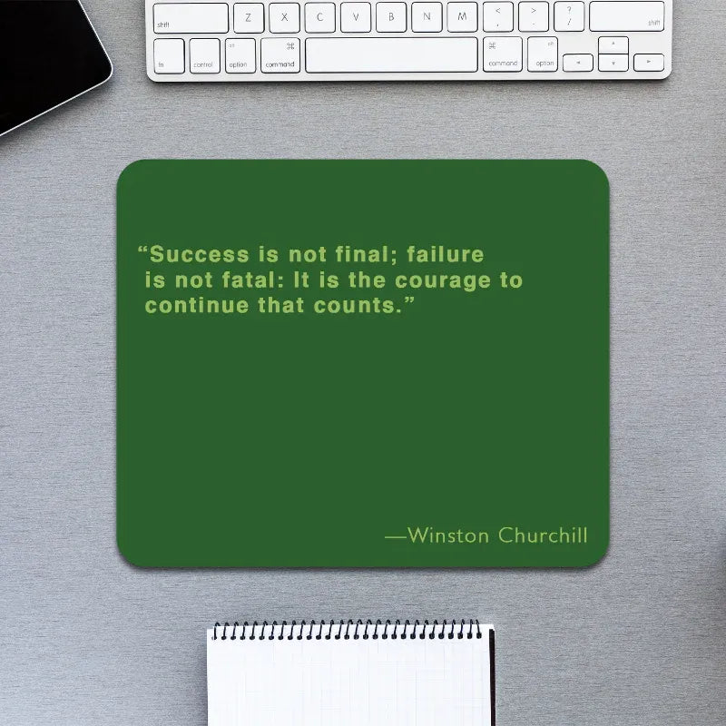 Green mouse pad with Winston Churchill quote on a desk with keyboard and notebook.