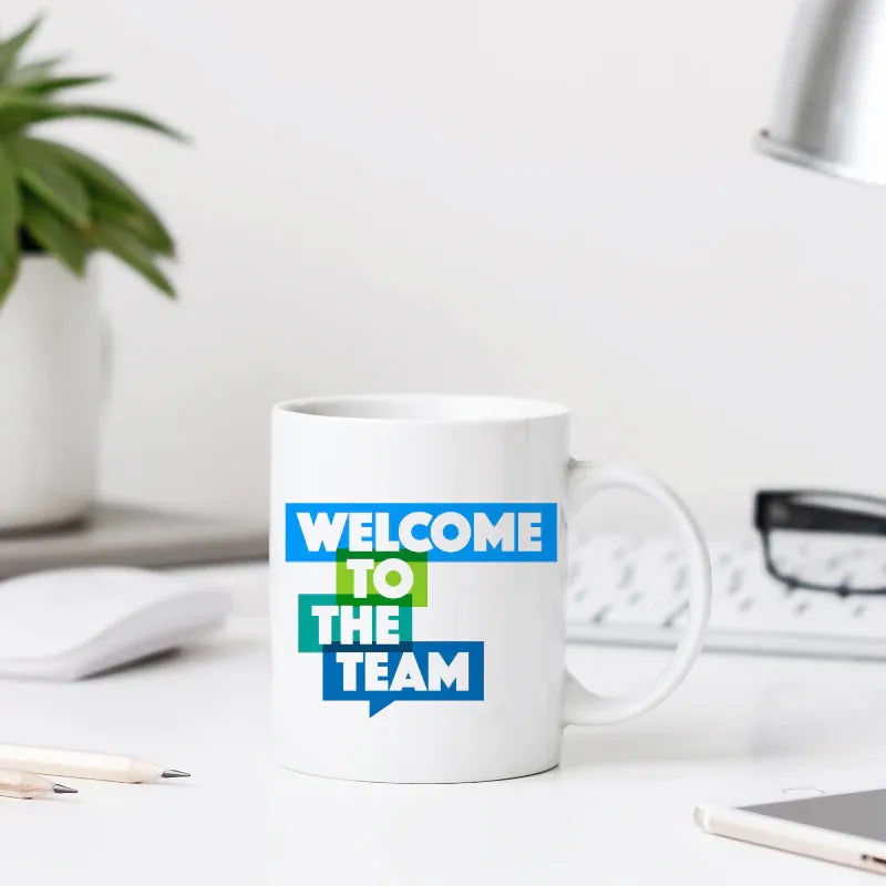 White mug with 'Welcome to the Team' text on a desk with office items.