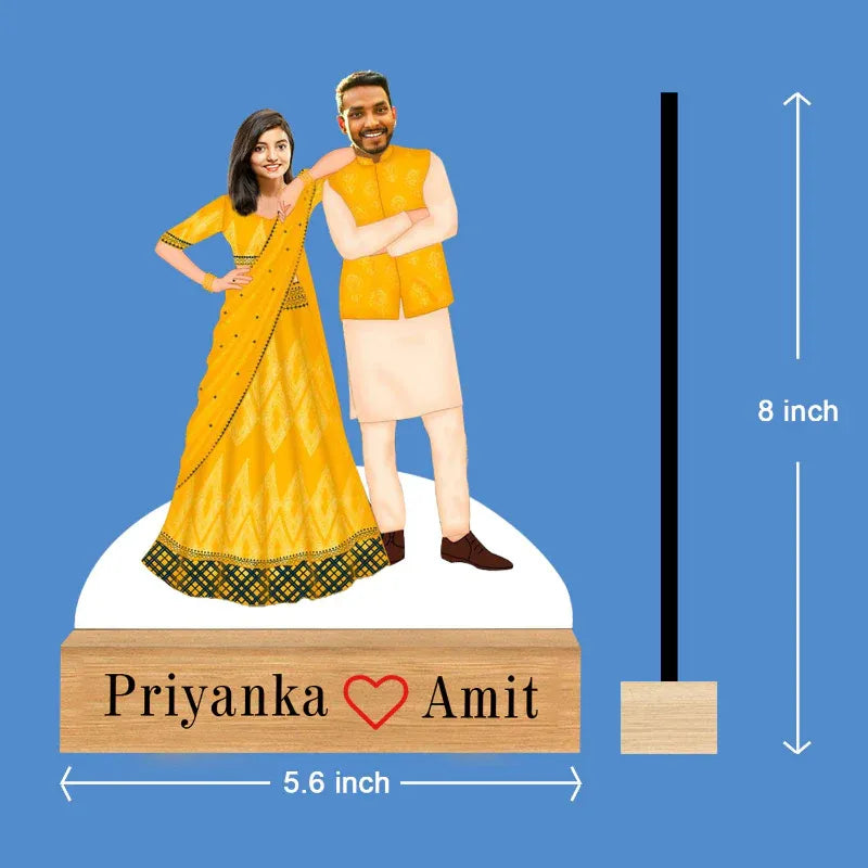 caricature of a couple in traditional attire with a wooden base displaying 'Priyanka Amit'.