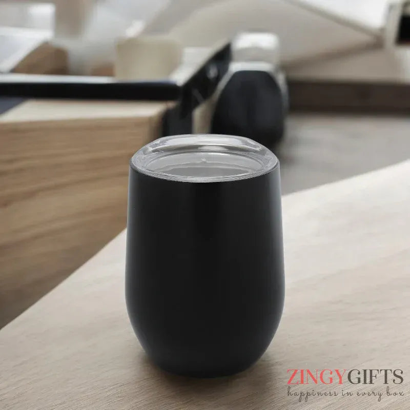 Black insulated tumbler on a wooden surface with a blurred indoor background