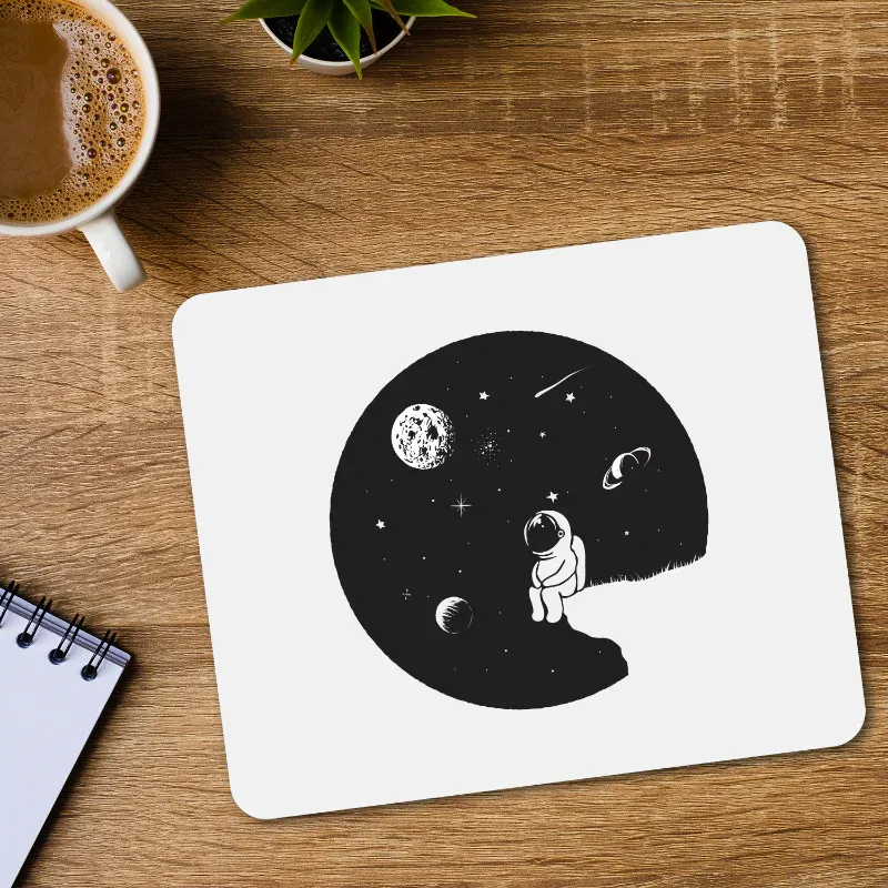 Mouse pad with space-themed design featuring an astronaut and celestial bodies on a wooden desk.