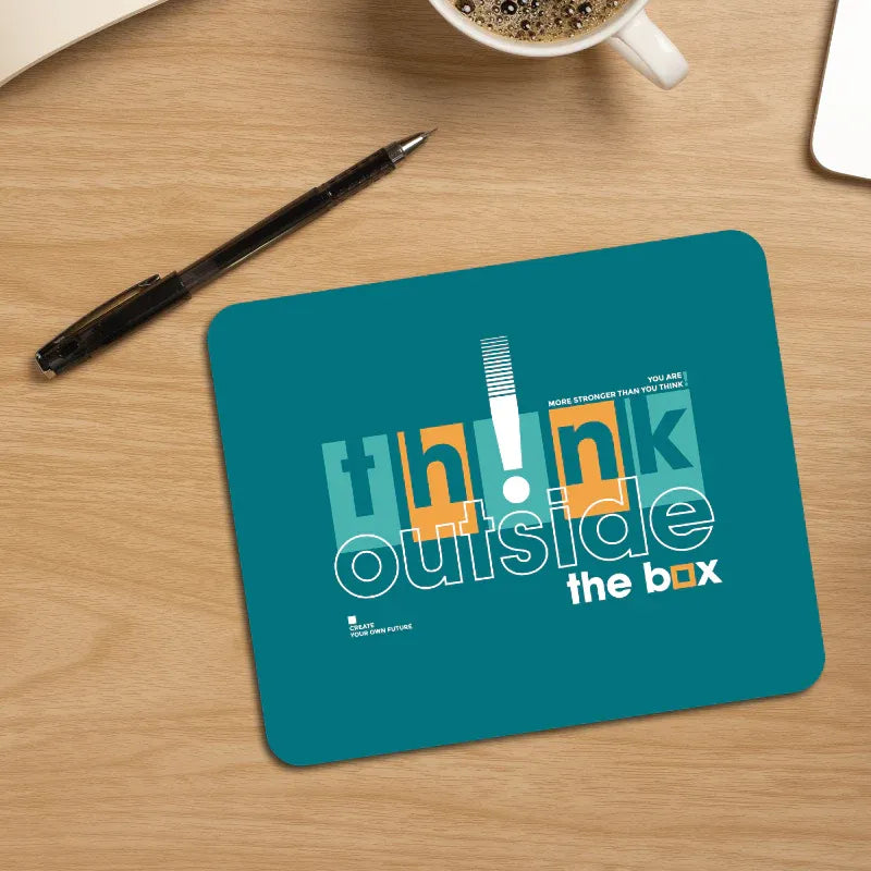 Teal mouse pad with 'think outside the box' text on a wooden desk with a pen and coffee cup.