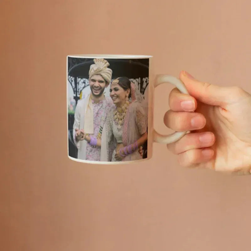 Person holding a mug with a printed photo of two people on a peach background