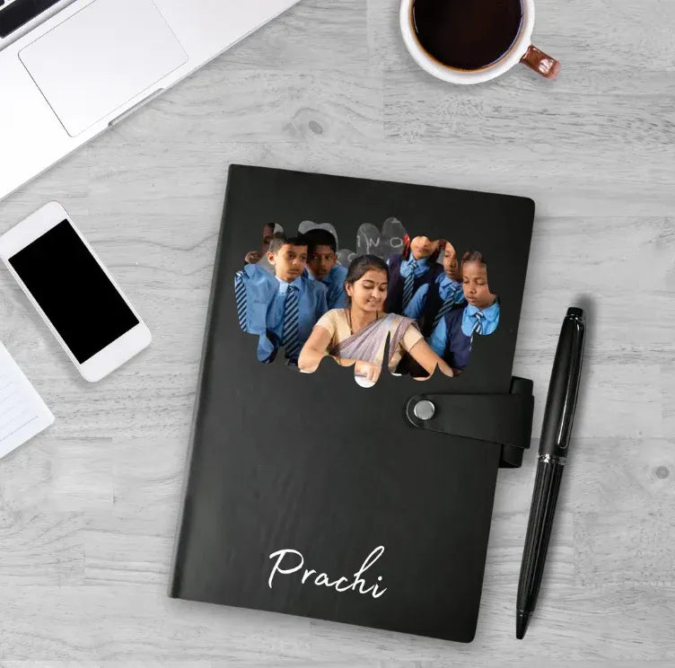 Black notebook with a personalized design on a desk with a phone, coffee, and pen.