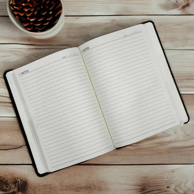 Open notebook on a wooden surface with a small plant in the corner.