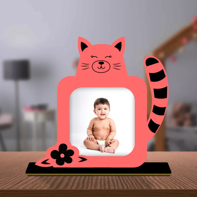 Pink cat-shaped photo frame with a baby photo inside, placed on a wooden surface.