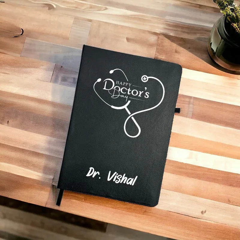 Black notebook with 'Happy Doctor's Day' and 'Dr. Vishal' on a wooden surface