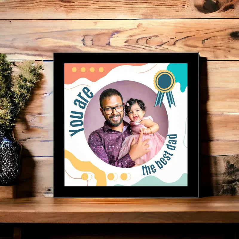 Framed photo of a man and a child with text 'You are the best dad' on a wooden surface.