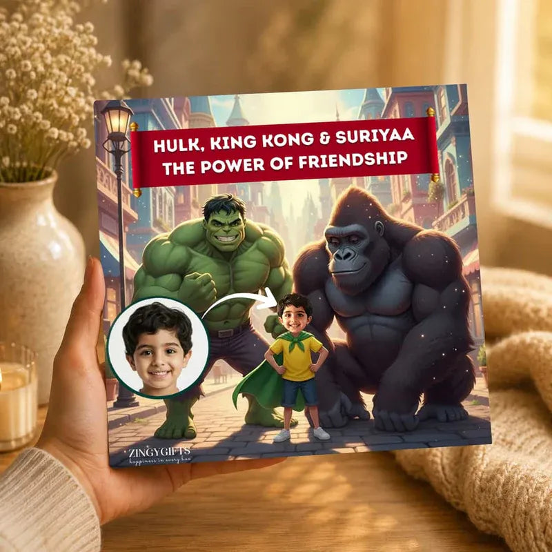 A hand holds a personalized children's book titled 'HULK, KING KONG & SURIYAA THE POWER OF FRIENDSHIP' featuring custom illustrations of Hulk, King Kong, and a boy named Suriyaa. The book cover includes a circular photo of the boy and is branded by Zingy Gifts.