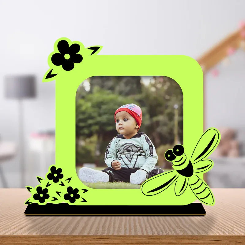 Cute baby photo frame gift — neon green bee and floral themed acrylic photo standee with custom baby photo, black wooden base, desk display on wooden surface.