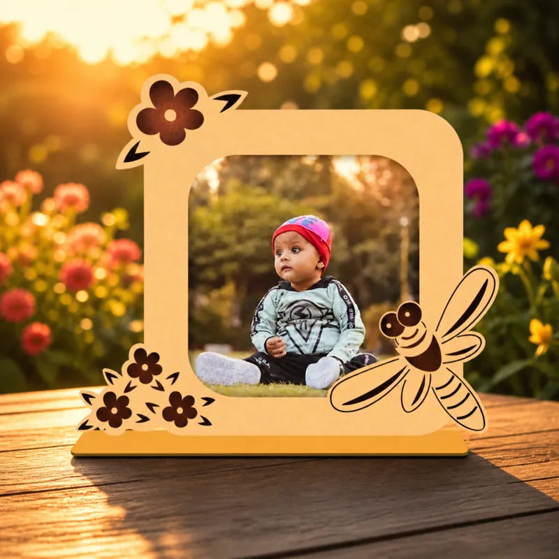 Wooden photo frame with floral and insect designs on a wooden surface with a blurred natural background