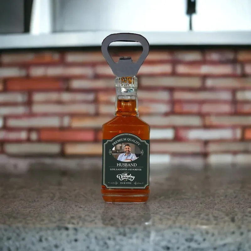 Personalized fridge magnet with a miniature bottle labeled 'Husband' on a countertop with a brick wall background.