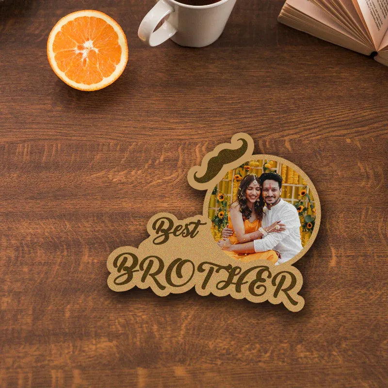 Wooden coaster with a photo of two people and 'Best Brother' text on a wooden surface with an orange and mug.