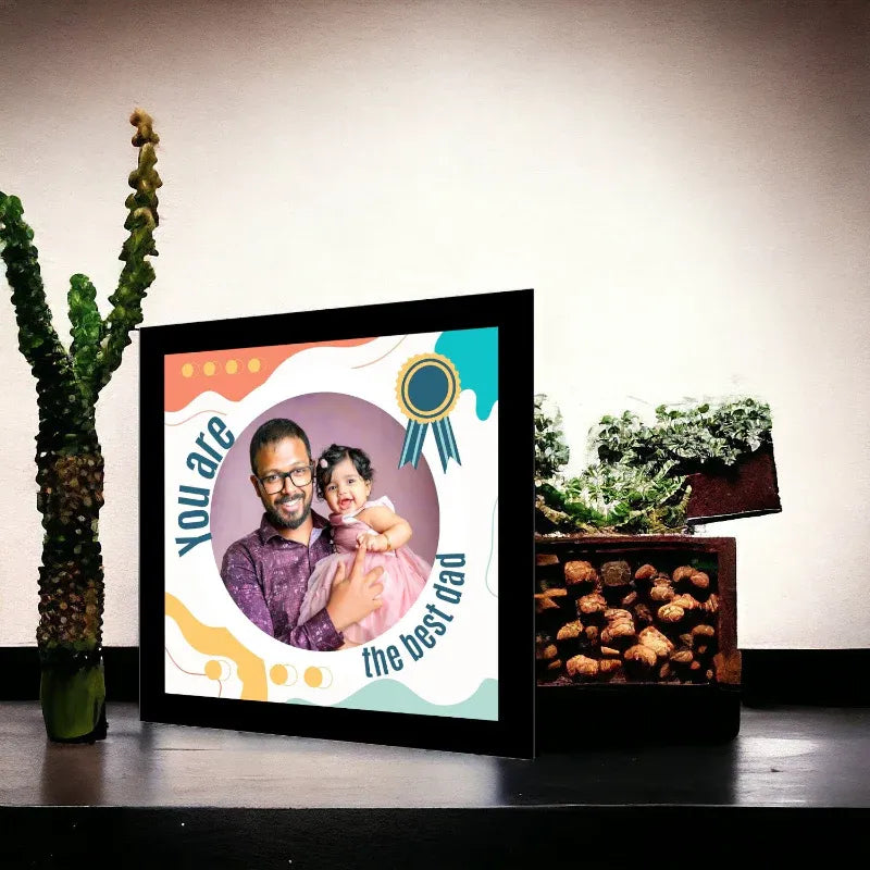 Framed picture of a man and a child with text 'You are the best dad' on a table with plants in the background.