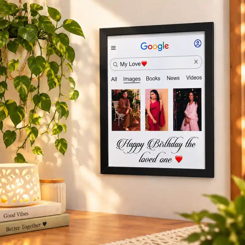 A white personalised google photo  frame wall art print hangs on a warm beige wall above a wooden table. The print displays a Google search result page with the search query 'My Love' and three photos of women, with 'Happy Birthday the loved one' written in script at the bottom.