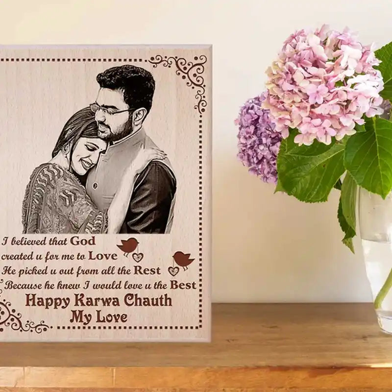 A personalized wooden engraved gift plaque featuring a photo of a couple, romantic text, and decorative borders, displayed on a wooden surface next to a vase of pink and purple hydrangeas.