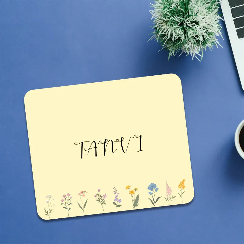 Yellow mouse pad with floral designs and 'TANV' text on a blue surface.