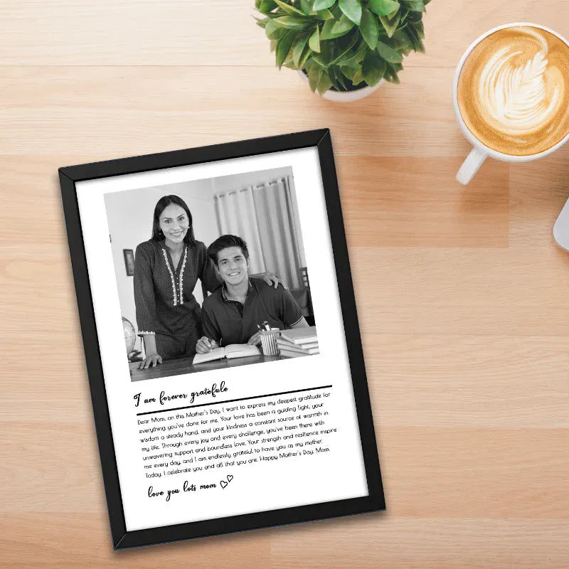 Framed black and white photo of two people with a heartfelt message on a wooden surface with a plant and coffee.