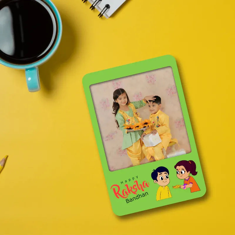 Green photo magnet frame with a picture of two children on a yellow background, featuring 'Happy Raksha Bandhan' text.