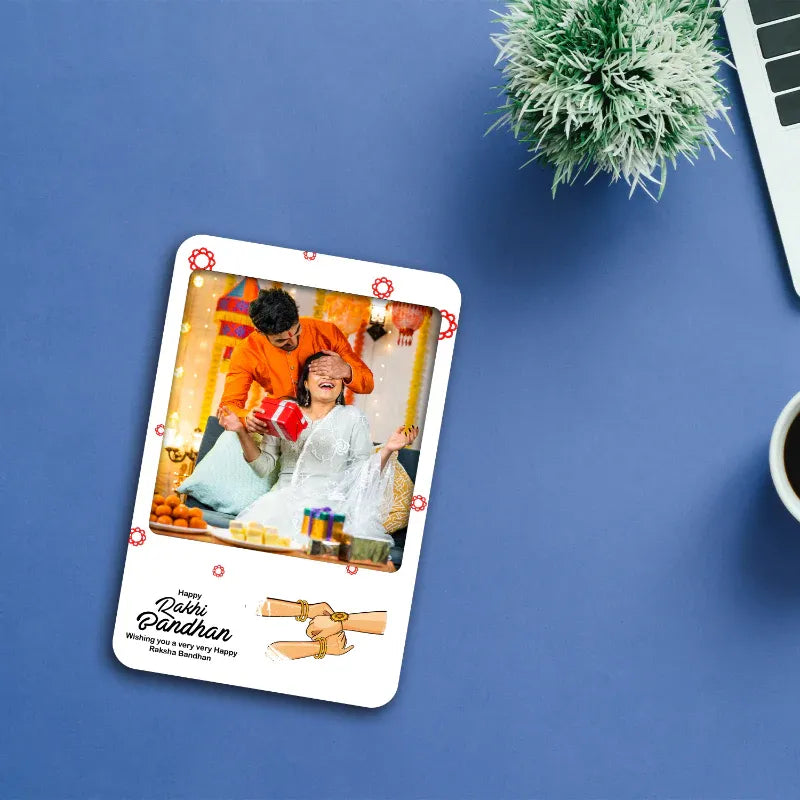 photo magnet with a printed photo of a brother and sister on a blue surface with a plant and laptop.