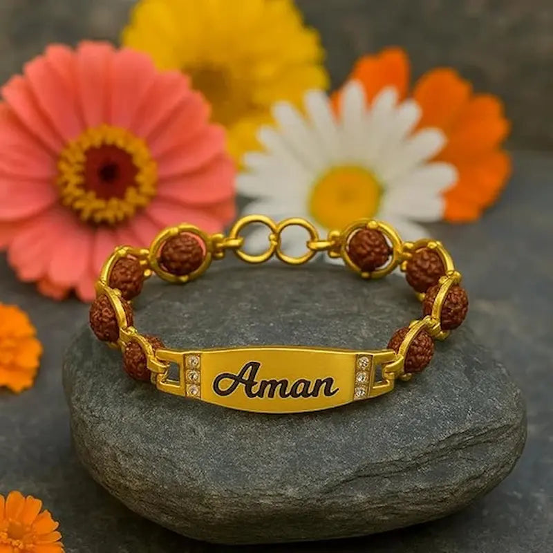 Gold bracelet with brown beads and 'Aman' engraving on a stone surface with flowers in the background