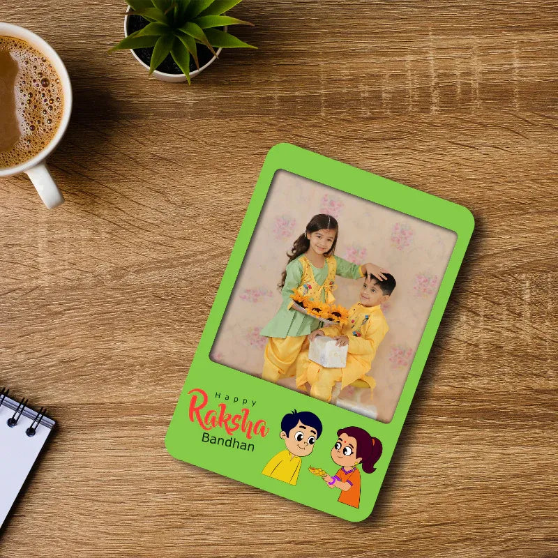 Green photo fridge magnet with a picture of two children on a wooden table with a cup of coffee and plant.