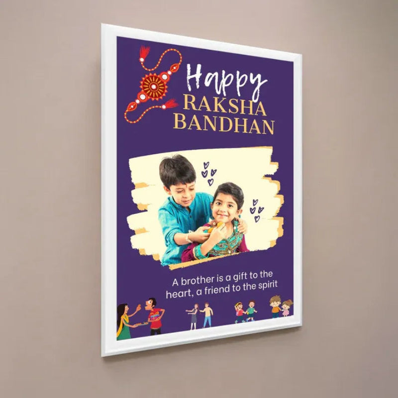 A framed personalized Raksha Bandhan poster hanging on a neutral beige wall. The poster features a deep purple background with 'Happy RAKSHA BANDHAN' in white and gold text, a decorative red and orange paper-knife motif, a central photo placeholder of a boy and girl, and small illustrations of children at the bottom.