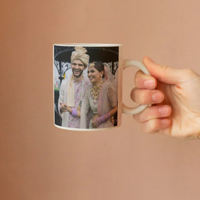 Person holding a mug with a printed photo of two people on a beige background