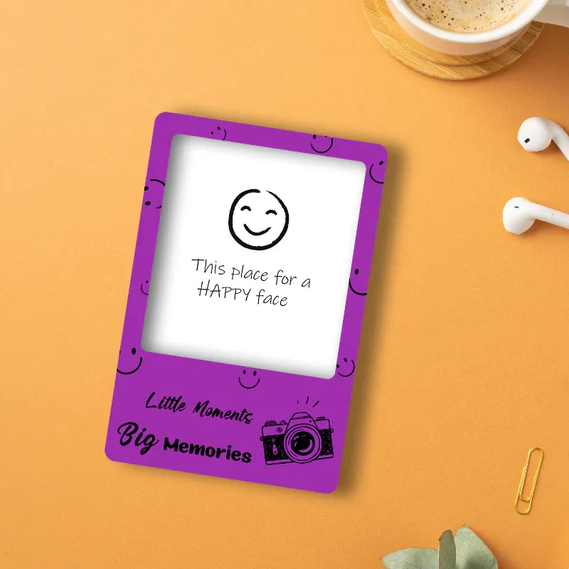 Purple frame with a white card featuring text and a smiley face on an orange surface with a cup and earbuds.