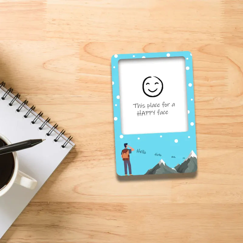 Small blue frame with a smiley face design on a wooden surface with a notebook and coffee cup.