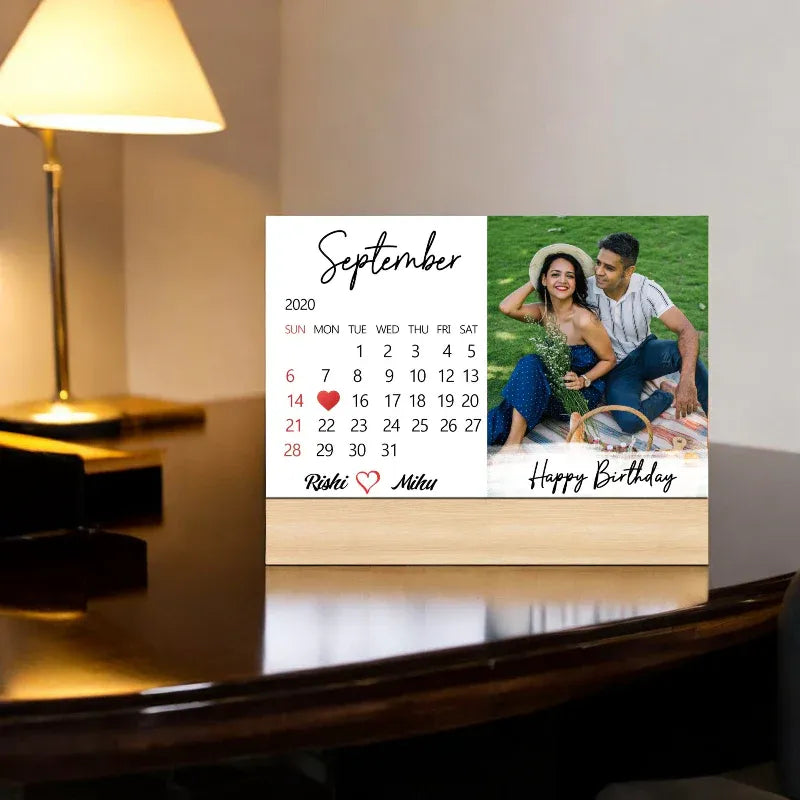 Calendar with a couple's photo and 'Happy Birthday' message on a wooden desk.