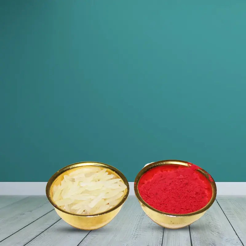 Two small gold bowls on a light wood surface against a teal background. The left bowl contains pale yellow powder, and the right bowl contains bright red powder.