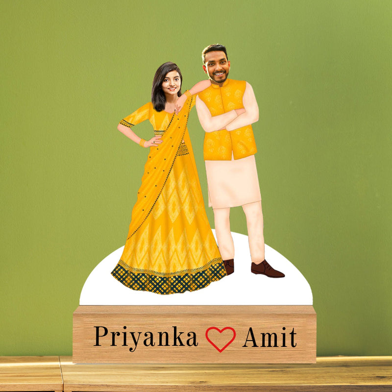 Figurine of a couple in traditional attire with a wooden base displaying 'Priyanka ❤️ Amit' on a green background.
