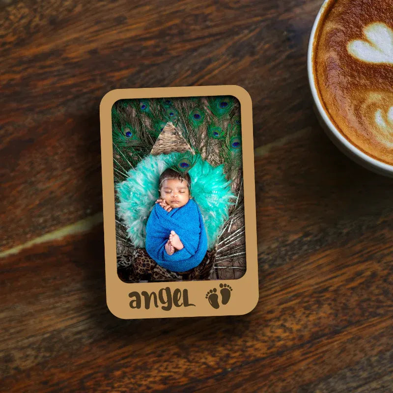 Wooden photo frame with a baby in a blue outfit and green blanket, next to a cup of coffee on a wooden table.