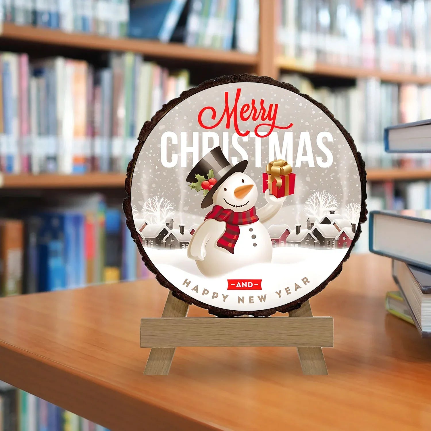 Christmas-themed decorative sign with a snowman on a wooden stand in front of a bookshelf.